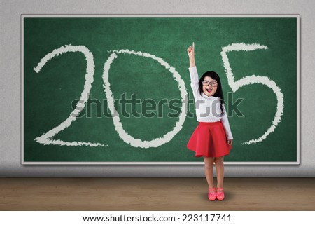 Sweet girl standing in class, raised her hand and forming number 2015
