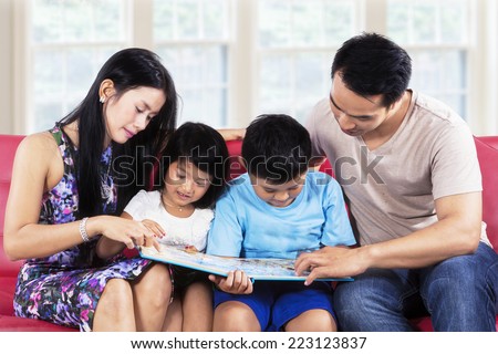 Four member of happy family read story book on sofa at home