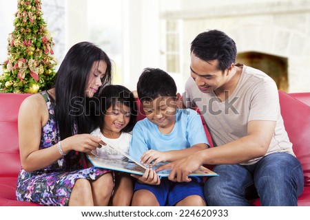 Portrait of happy family holding and read a story book together at home in christmas day