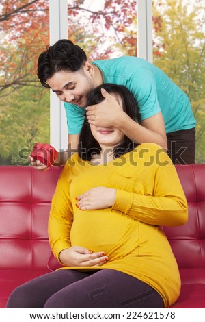 Portrait of young husband giving a present to his pregnant wife at home in autumn day