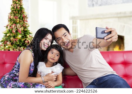 Portrait of asian family sitting on sofa and use a smartphone to take a self photo together