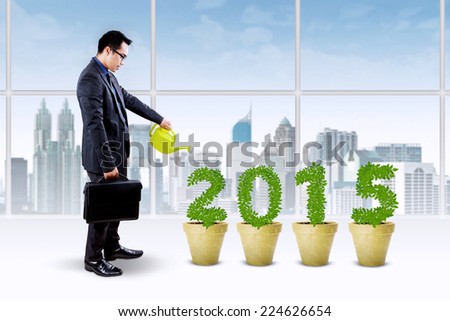 Young businessperson watering the trees shaped number 2015, symbolizing investment plan for the future 2015
