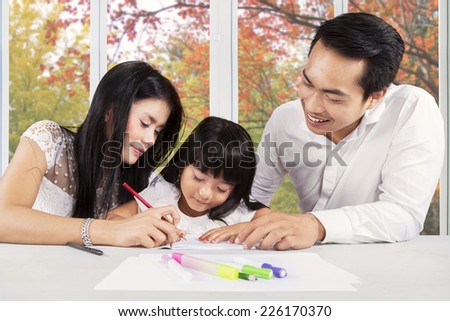 Portrait of two parents help their daughter doing homework at home in autumn day