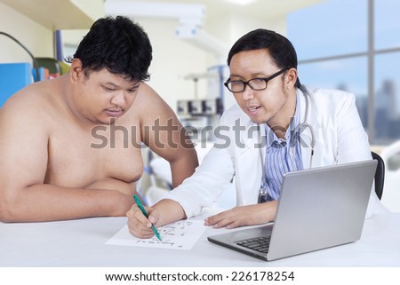 Young asian doctor writes a prescription for a fat man patient in hospital