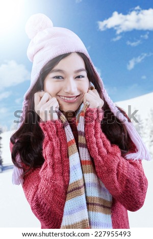 Attractive young girl in knitted clothes with hands grabbing the scarf. Looking at camera