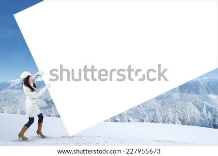 Young woman wearing winter clothes and pulling empty banner for copyspace, shot outdoors