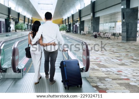 Two people walking on escalator while carrying a luggage in the airport hall