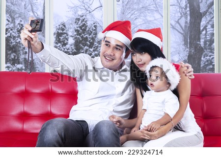 Asian father holding a digital camera to take picture with his family at home in christmas day