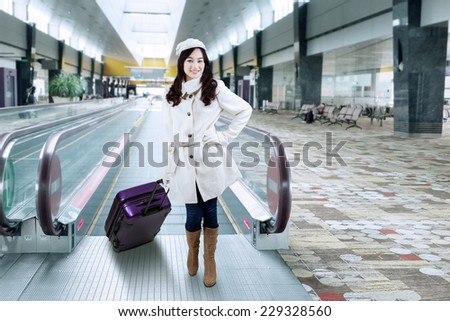 Portrait of beautiful woman standing in the airport hallway while wearing winter coat and carrying luggage