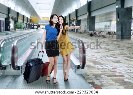 Portrait of two beautiful women looking and pointing something in the airport hall