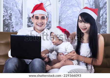 Joyful family wearing christmas hat and smiling on the camera while using laptop computer on sofa