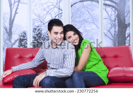 Portrait of happy woman sitting on a red sofa and hugging boyfriend from the back