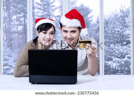 Portrait of man in santa hat holding credit card and use laptop for shopping online with his wife at home