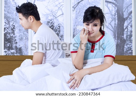 Young woman crying on bed and sitting separately with her husband after quarreling