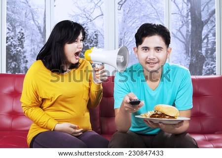 Portrait of pregnant woman yelling with a megaphone on her husband at home with winter background
