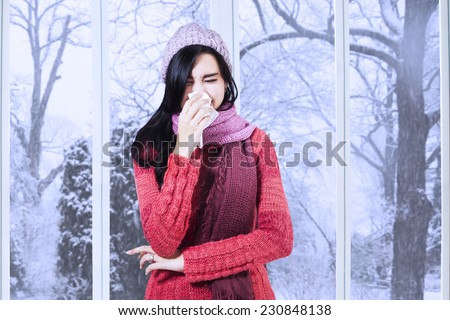 Young girl having flu and blowing her nose at handkerchief, shot at home in winter day