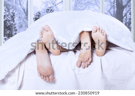 Closeup of human feet sleeping together on the bedroom with winter background on the window