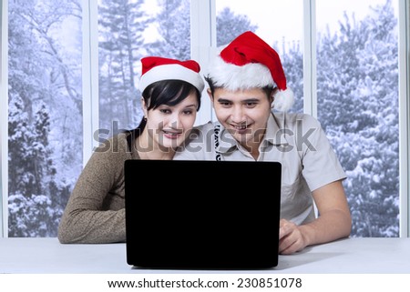 Young asian couple wearing christmas hat and using laptop computer for searching something on the internet
