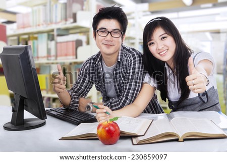 Happy student couple showing thumbs-up with computer on the desk