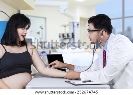 Asian doctor using stethoscope for listening the heartbeat his pregnant patient in hospital