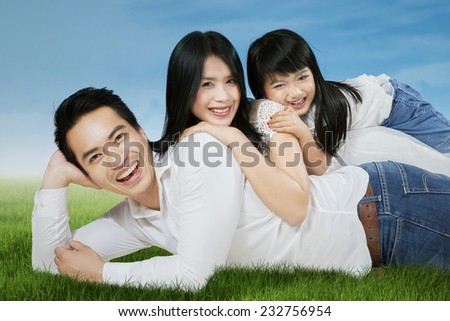 Happy asian family lying on grass and looking at camera, shot outdoors