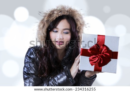 Lovely teenage girl in winter clothing, holding a presents with red ribbon