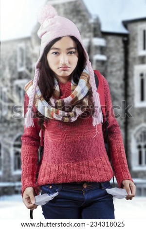 Sad female student having financial problem and showing empty pockets near the school building