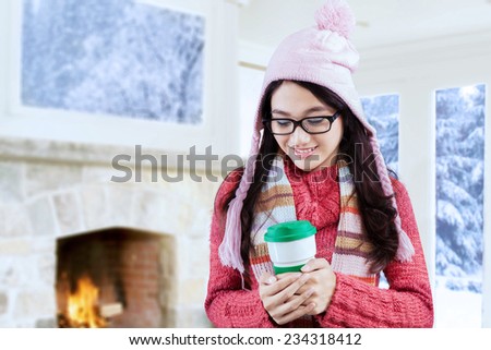 Sweet young woman wearing winter knitted clothes and enjoy hot drink in a disposable cup at home