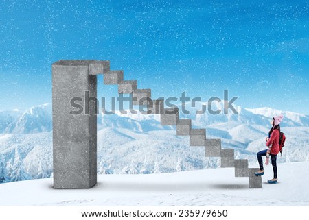 Young girl in winter clothes carrying backpack and climbs the stairs on the mountain at snowy day