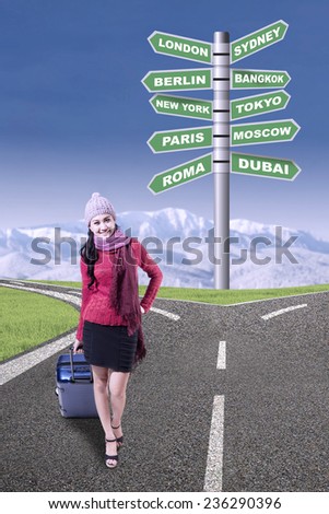 Beautiful woman in winter clothes holding suitcase on the road