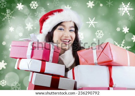 Portrait of cheerful girl with santa hat, smiling at the camera while holding many surprise gifts