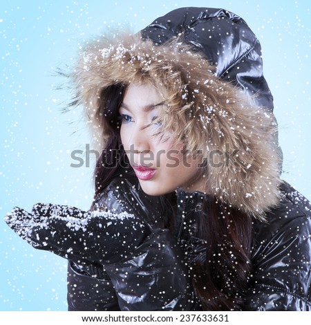 Portrait of pretty lady with winter clothing, holding cold snow on her palms and blowing its