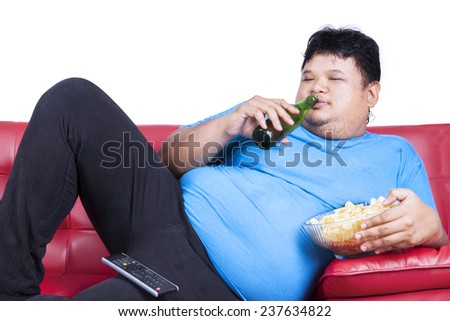 Overweight man sitting lazy on sofa while drinking beer and eat snack Overweight man sitting lazy on sofa while drinking beer and eat snack