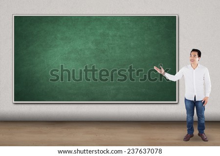 Full length of casual man standing in the class and showing blank chalkboard