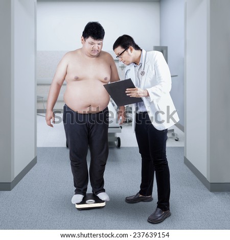 Male doctor make a note of the body mass of overweight man on a clipboard