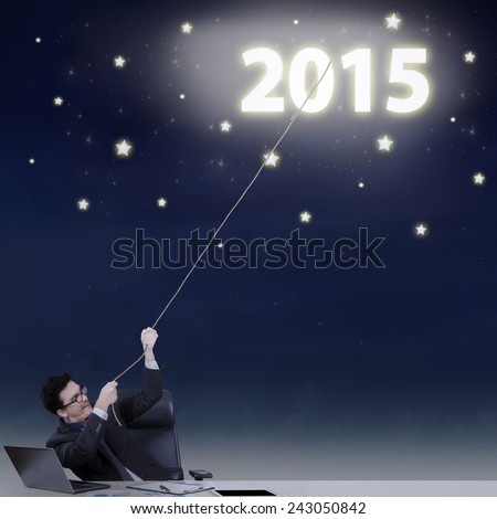 Young businessman try to pull numbers 2015 from the sky, symbolizing high business target in 2015