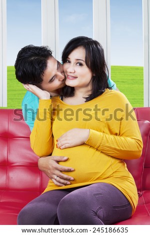 Portrait of romantic husband kissing his pregnant wife cheek at home