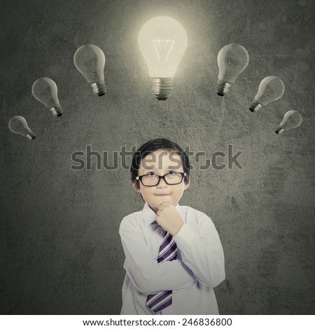 Portrait of cute little boy with thinking style while looking at the bright lightbulb