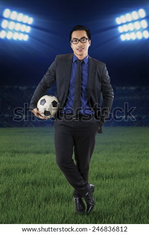 Full length of a young businessman standing at field while holding a soccer ball