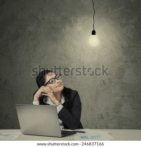 Female asian manager working on desk with laptop and paperwork looking at bright lightbulb