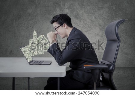 Cheerful caucasian businessman looking money dollars from laptop comoputer