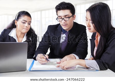 Portrait of young businessman meeting with two female partners, reading and signing a document