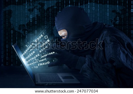 Side view of unknown hacker with mask stealing information from laptop computer