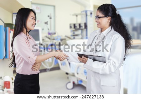 Portrait of young doctor shaking hands with chinese patient in the hospital
