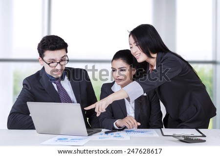 Portrait of chinese businesswoman pointing at the laptop and explain documents to her colleague