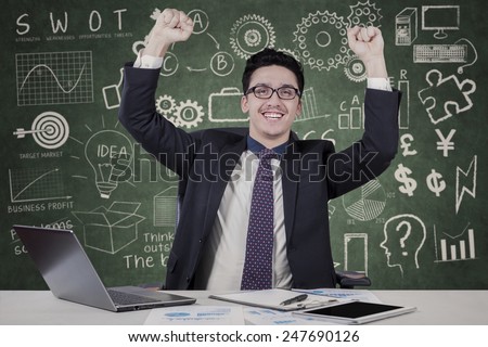 Portrait of successfull caucasian businessman celebrate his success with doodles on blackboard