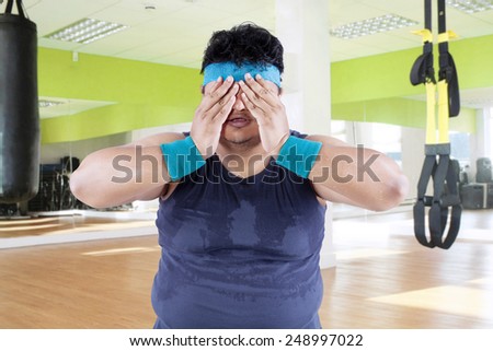 Fat man tired after workout and covering his face