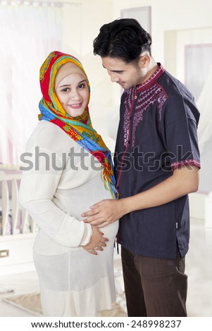 Attractive pregnant woman and her husband standing in the bedroom