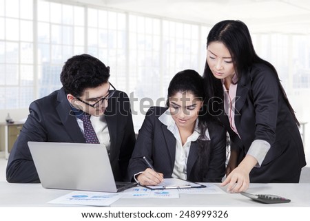 Female entrepreneur signing a business contract with two partners looking her