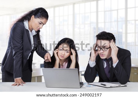 Bossy businesswoman pointing at laptop to show the mistake of her employees